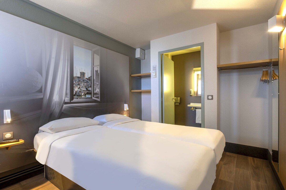 A hotel room with a large bed, a mirror, a wardrobe, and a view of a marina.