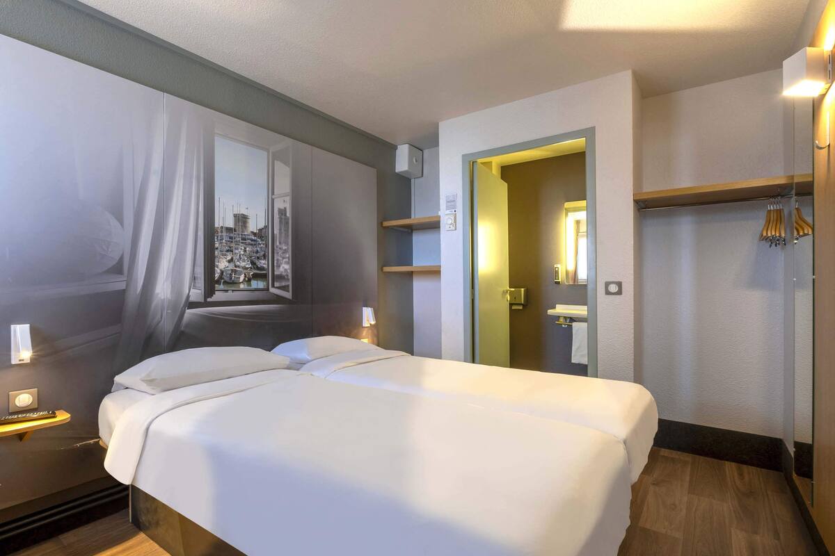 A hotel room with a large bed, a mirror, a wardrobe, and a view of a marina.