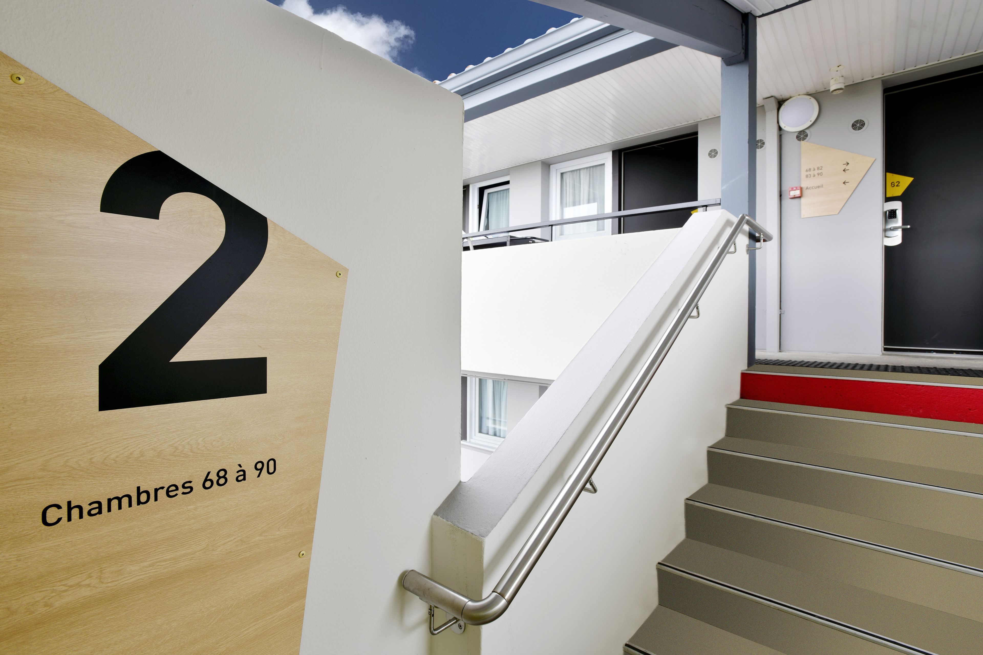 A staircase with a handrail, a wooden door with the number 2, and a sign indicating rooms 68 to 90.