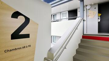 A staircase with a handrail, a wooden door with the number 2, and a sign indicating rooms 68 to 90.