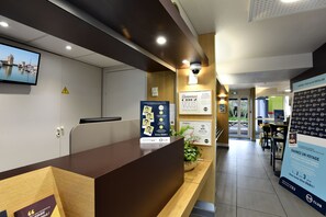 A reception desk with a monitor, a welcome sign, and a signboard advertising a hotel club. - B&B Hotel La Rochelle Angoulins sur mer (Angoulins)