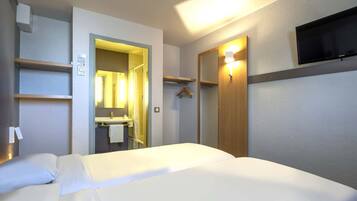 A hotel room with a bed, a mirror, a TV, and a bathroom visible through an open door.