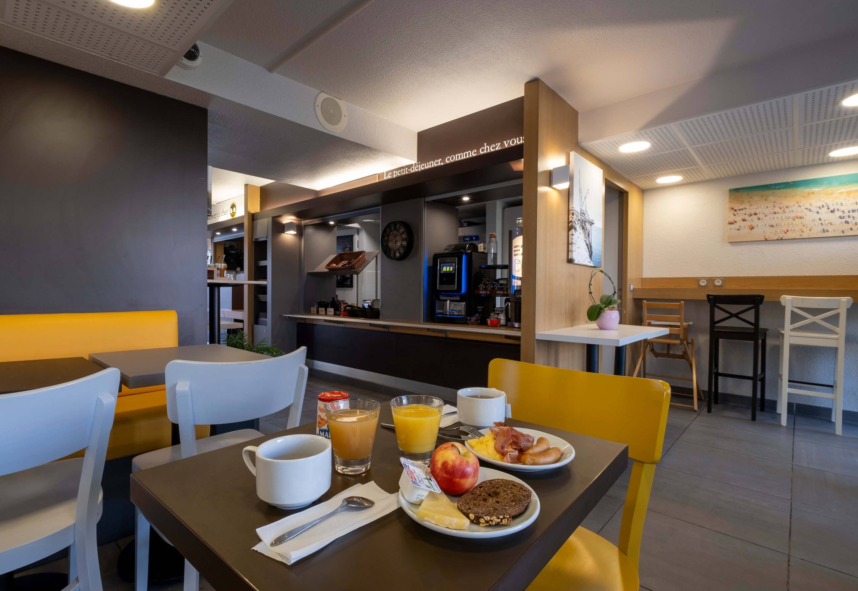 A breakfast setup with a coffee machine, fruit, and eggs on a table in a modern cafe.