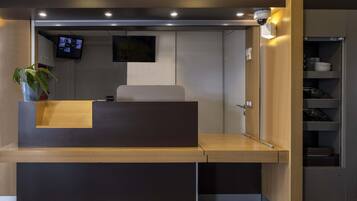 A reception desk with a flat-screen TV mounted above it, a potted plant to the left, and a wooden counter.