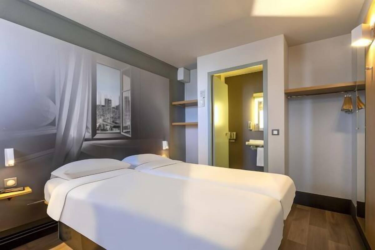 A hotel room with a bed, a nightstand, a mirror, a wardrobe, and a door leading to a bathroom.