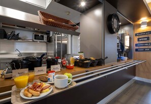 A breakfast bar with a variety of food items, including toast, eggs, bacon, and fruit. There are also two glasses of orange juice and a coffee cup.