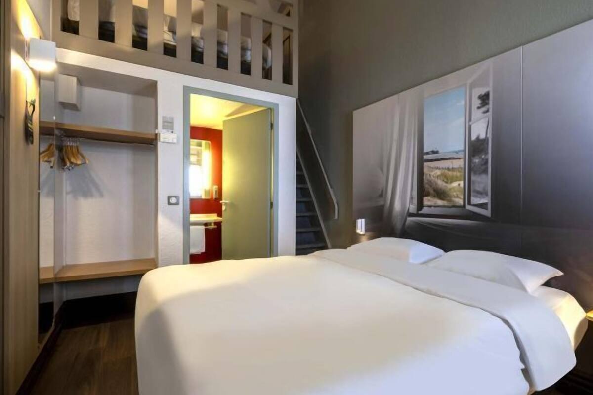 A hotel room with a bed, a wardrobe, a mirror, and a painting on the wall.