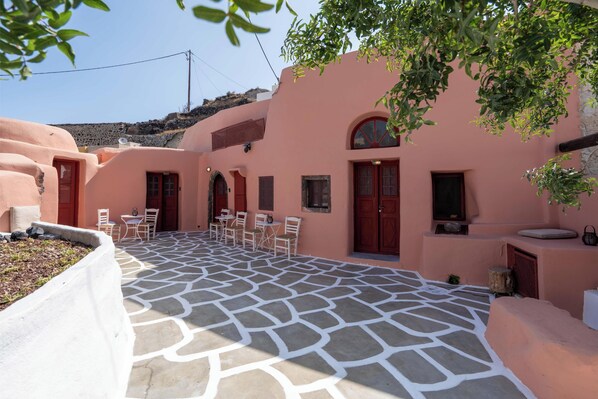 A courtyard with a stone floor, pink walls, and a seating area with chairs and tables. - Elyvia Caves (Oia)