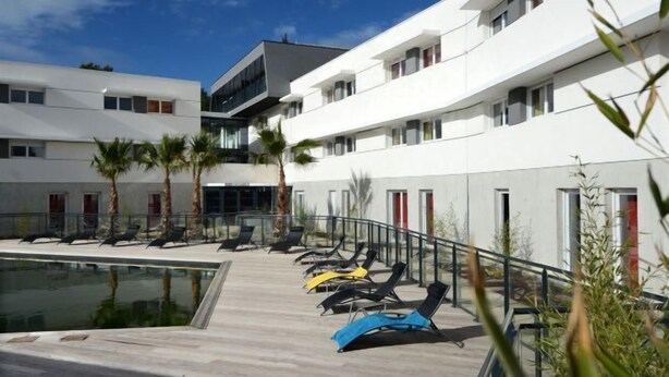 A modern hotel with a pool area, sun loungers, and palm trees. - Residence le Terral - Vacancéole (Saint-Jean-de-Vedas)