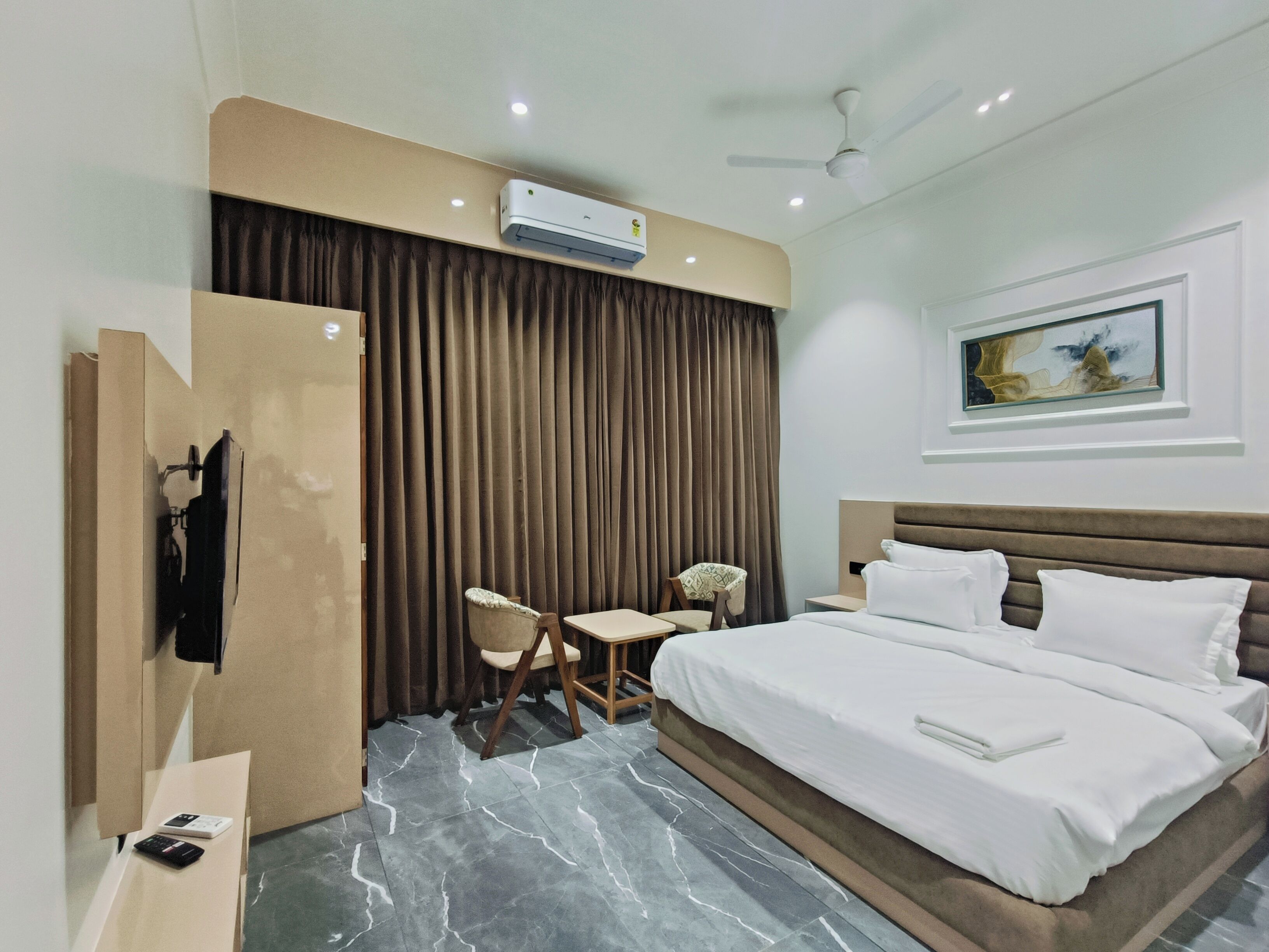 Una habitación de hotel con cama, escritorio, silla, aire acondicionado y un cuadro en la pared.