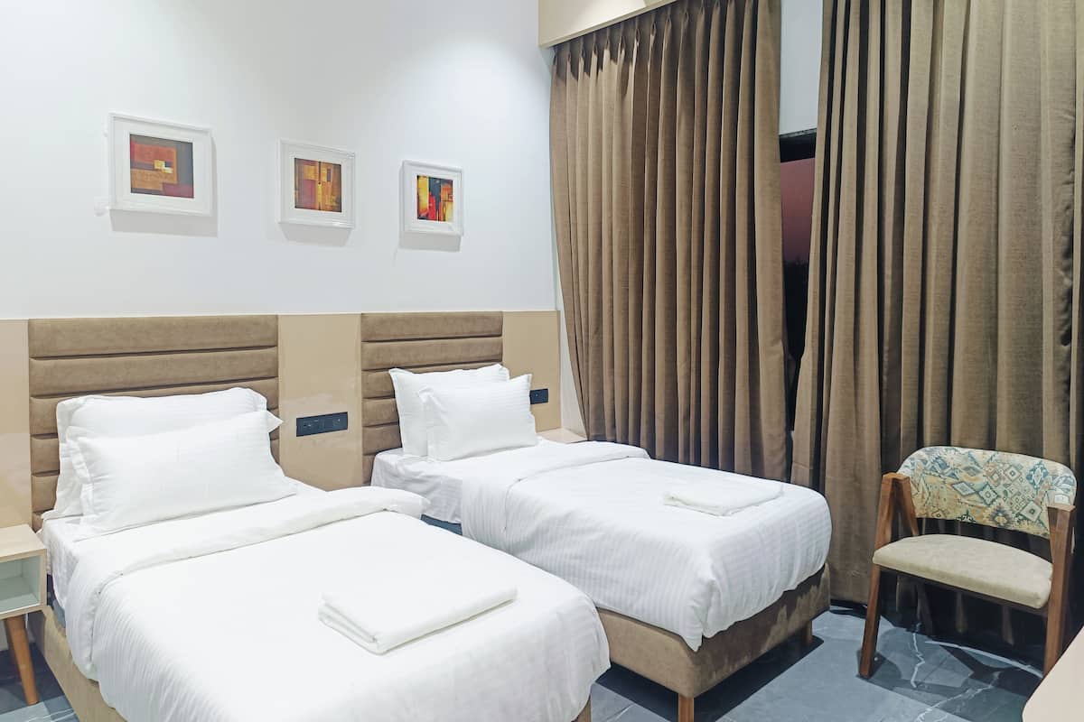 A hotel room with two beds, a chair, and three framed artworks on the wall.