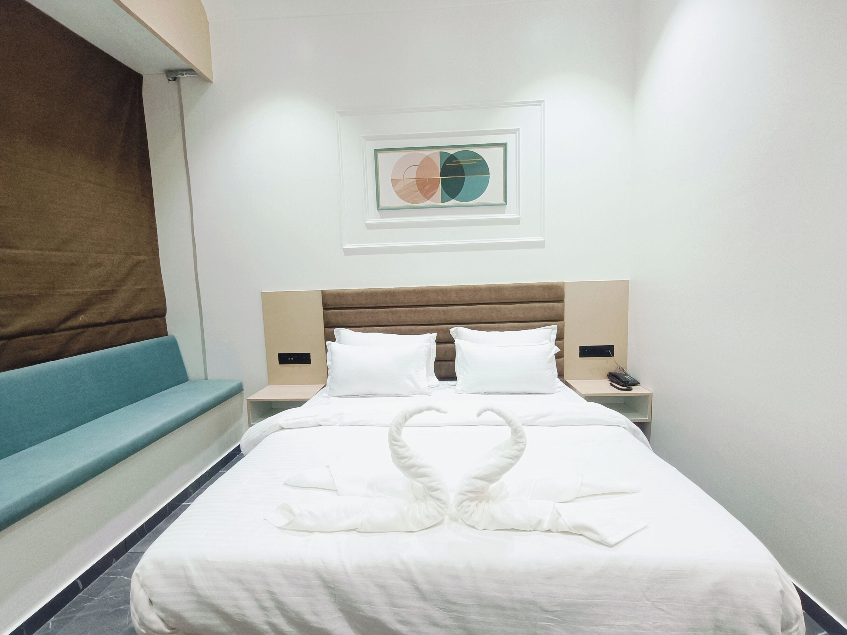 Een hotelkamer met een bed, een blauwe bank, een aan de muur hangend kunstwerk en een nachtkastje met een telefoon.