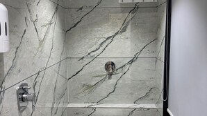 A modern bathroom with a marble floor, a white toilet, a shower area, and a built-in sink. - Hotel the octave (Surat)