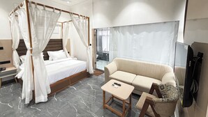 A modern bedroom with a four-poster bed, a sofa, a small table, and a TV. - Hotel the octave (Surat)