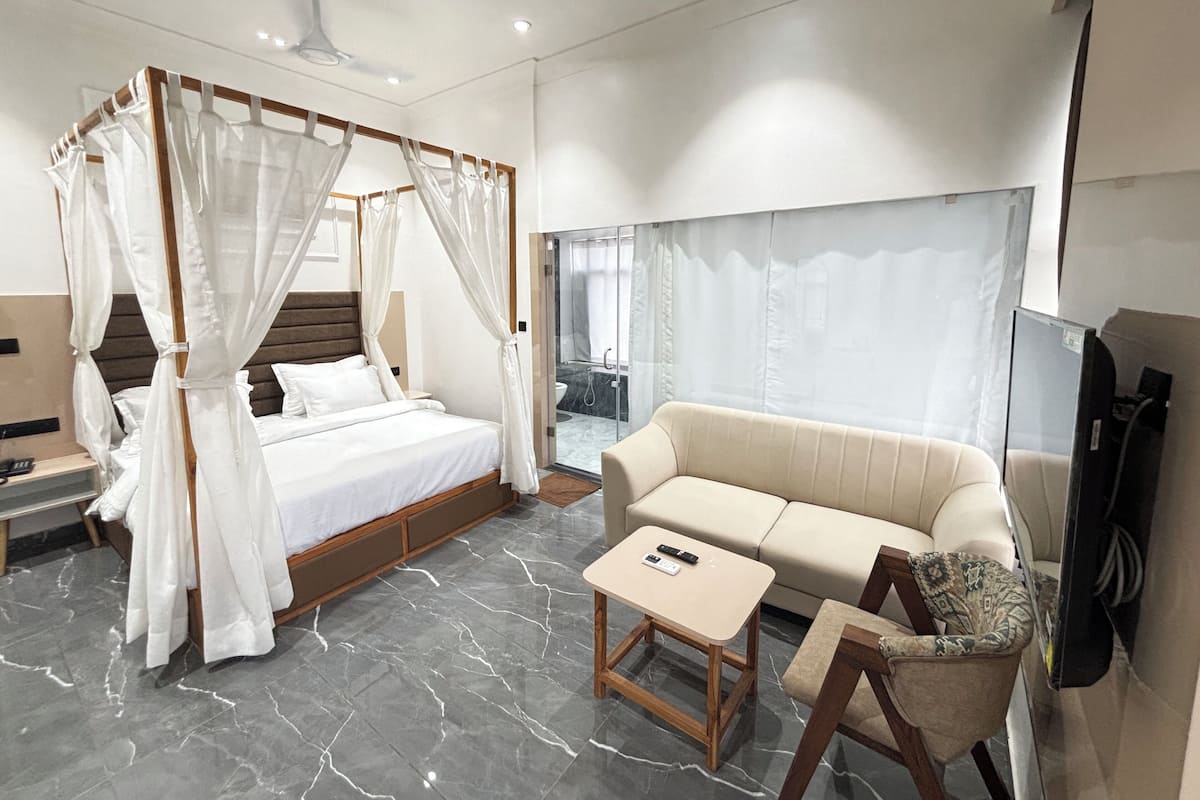 A modern bedroom with a four-poster bed, a sofa, a small table, and a TV.