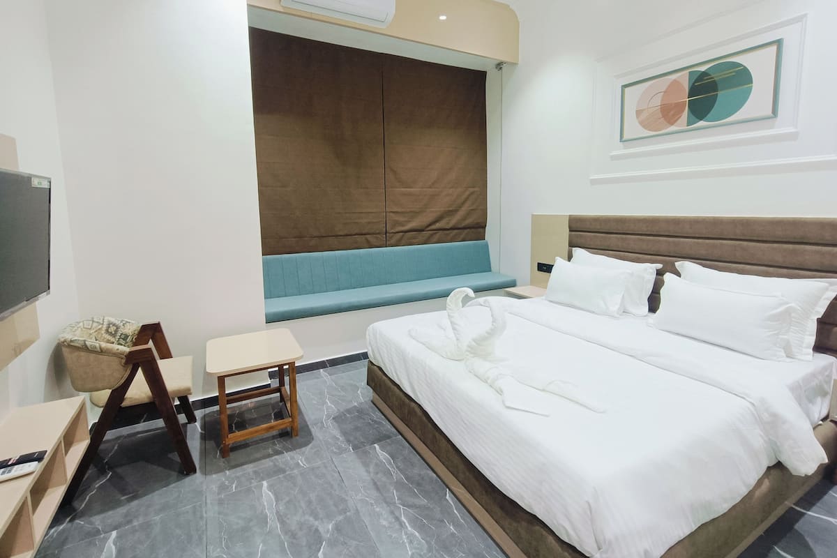 A hotel room with a bed, a small table, a chair, a TV, and a window with a brown blind.