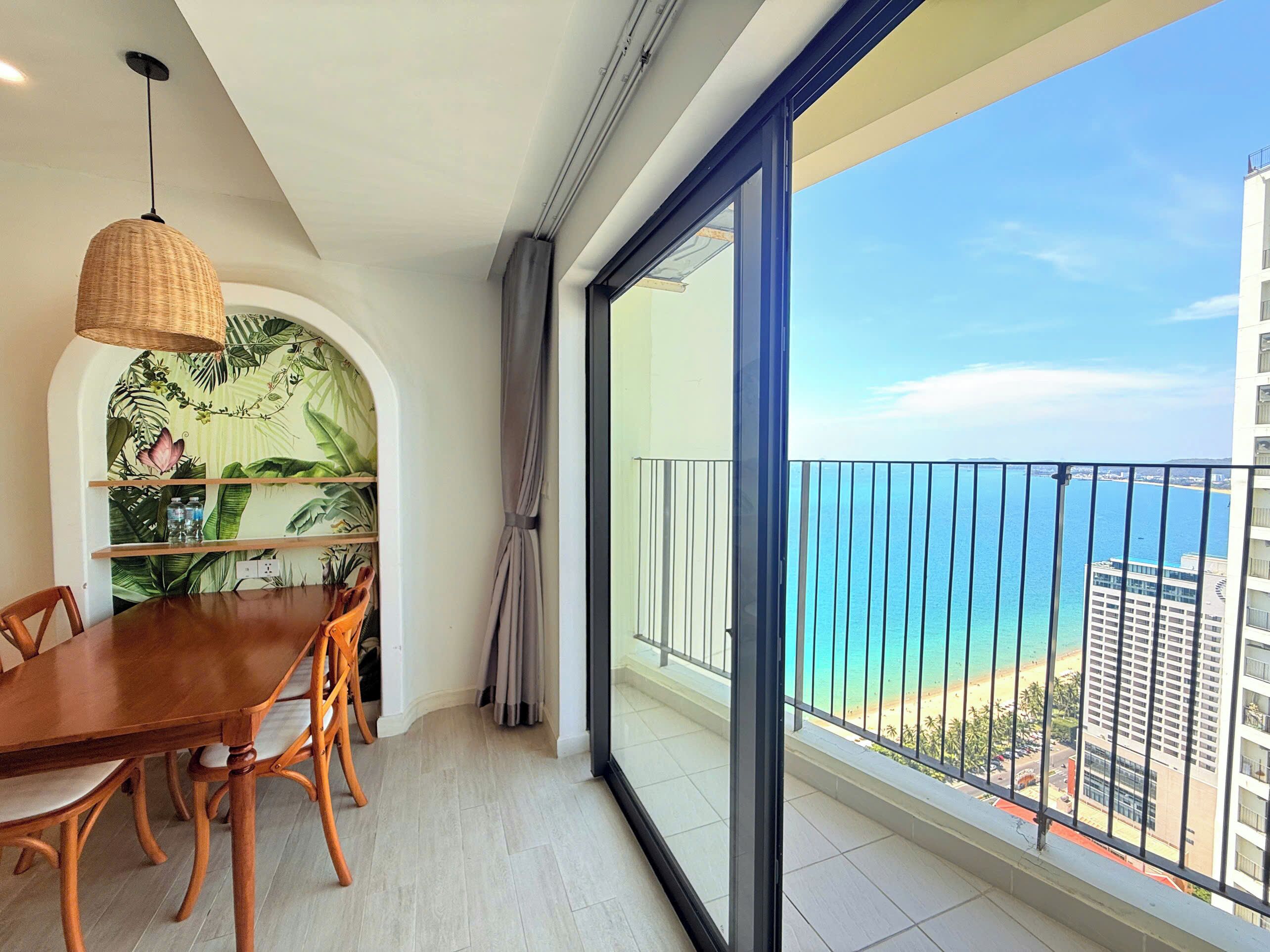 A balcony with a view of the sea and buildings, a dining area with a table and chairs, and a hanging light fixture.