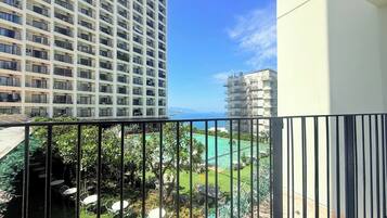 A balcony with a view of a swimming pool, a high-rise building, and a clear sky.
