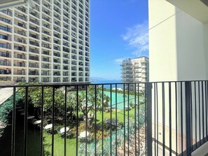 A balcony with a view of a swimming pool, a high-rise building, and a clear sky.