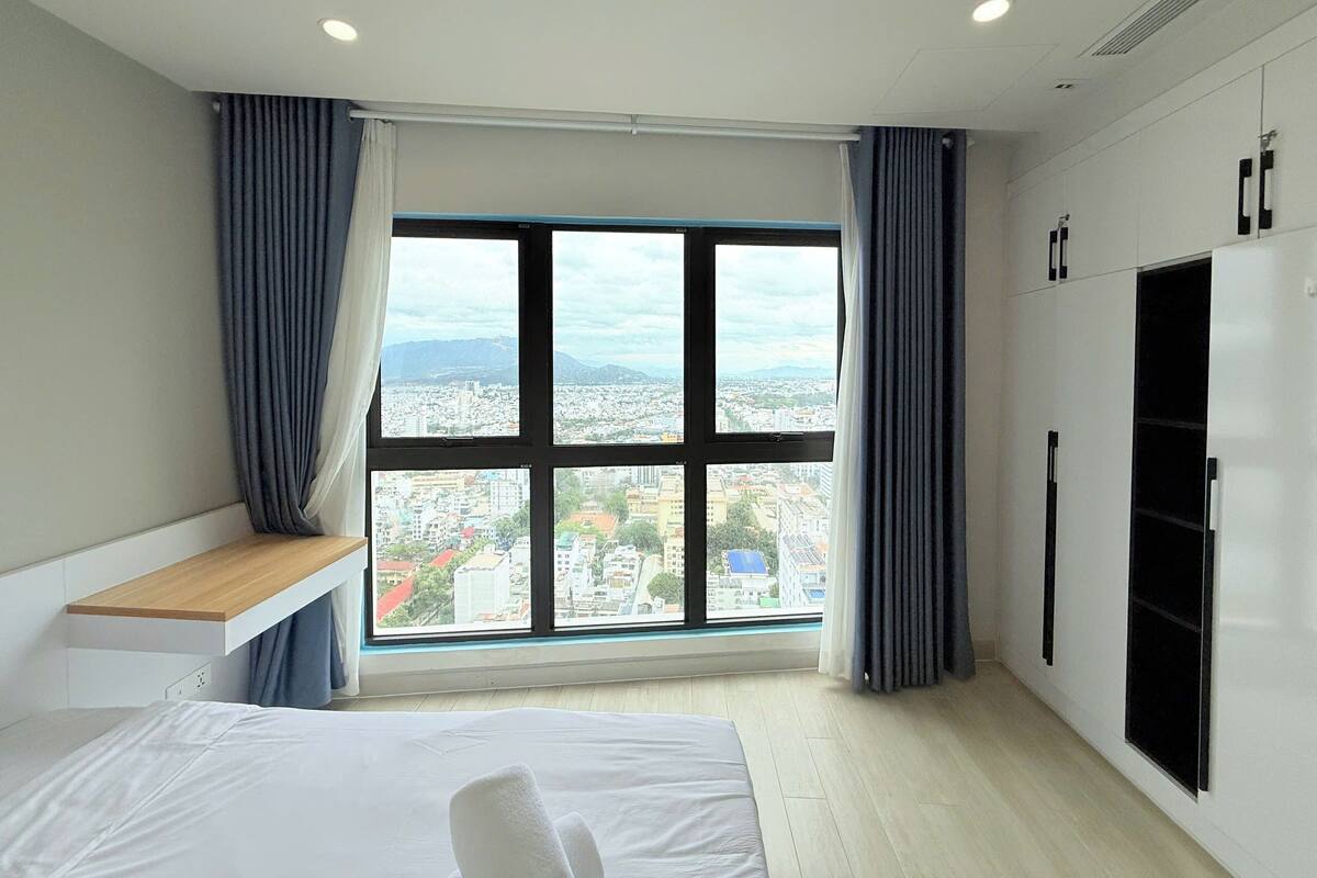 Habitación de hotel moderna con un amplio ventanal que ofrece vistas a la ciudad, una cama, un escritorio y un armario.