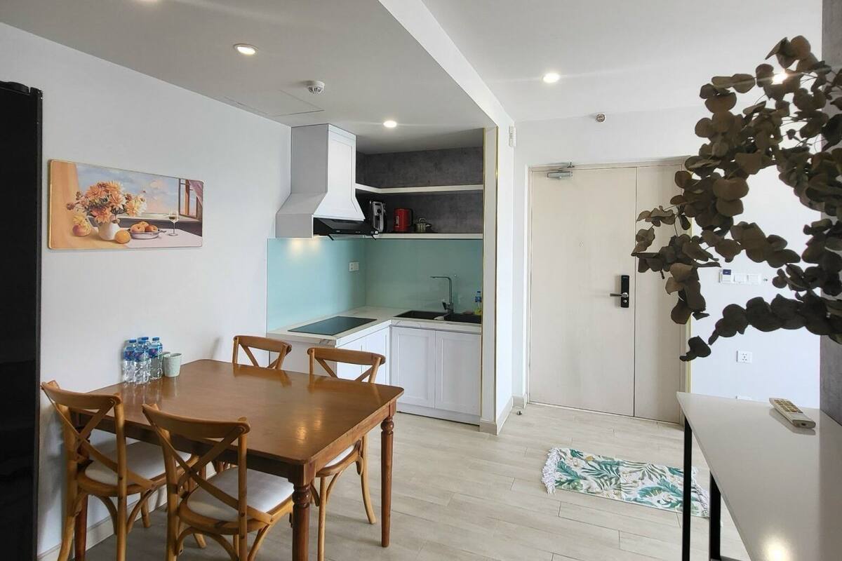 Una cocina moderna con armarios blancos, horno integrado y pileta. Hay una zona de comedor con mesa y sillas de madera.