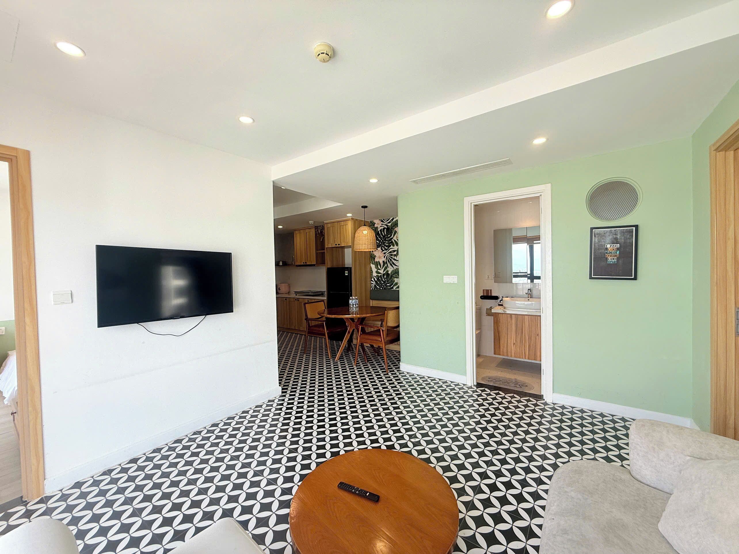 A modern living room with a flat-screen TV, a round wooden coffee table, and a patterned floor.