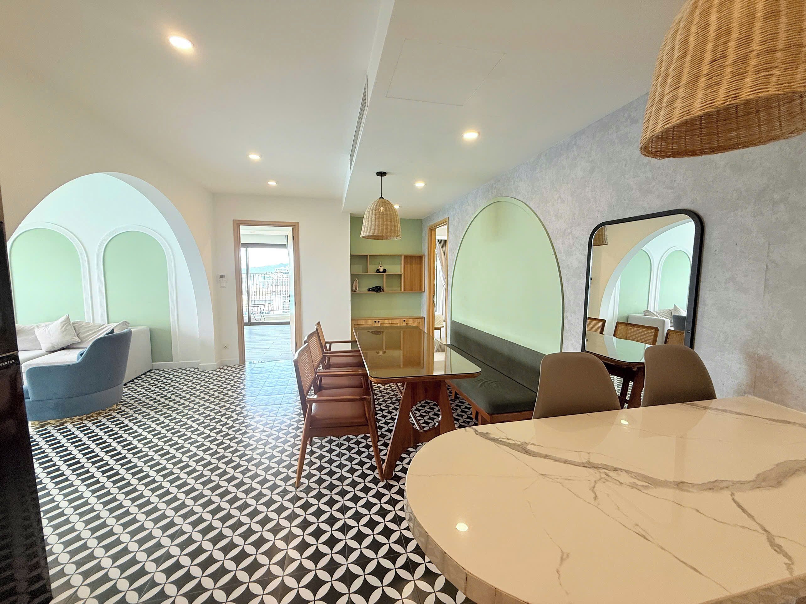 Una habitación de hotel con comedor, cama con cabecera, piso estampado y un espejo grande.