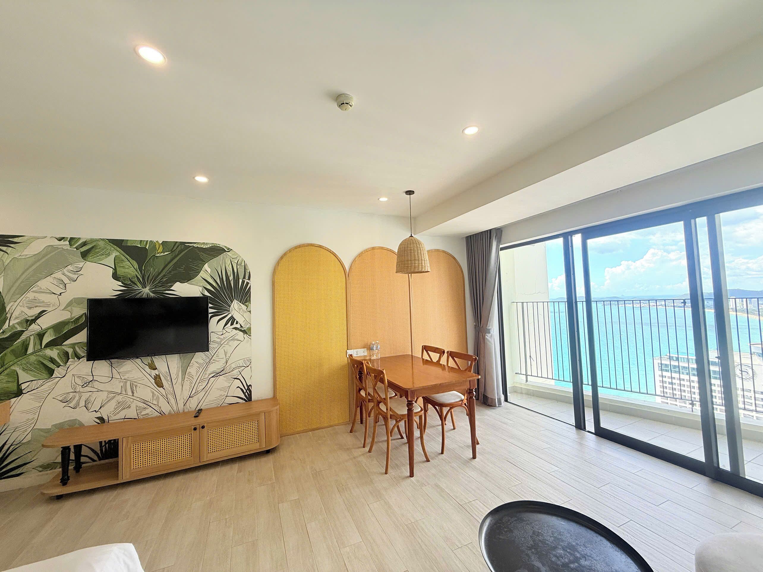 Una sala de estar moderna con comedor, un ventanal con vistas al mar y un televisor montado en la pared.