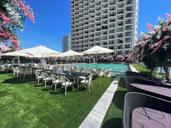 A rooftop pool area with white umbrellas, lounge chairs, and a view of a tall building.