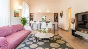 Un salon moderne avec un canapé rose, une table basse ronde et un téléviseur placé à droite.