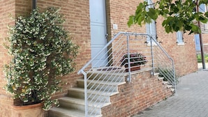 Ein Backsteinhaus mit weißer Tür, einer Treppe mit Metallgeländern und einem Blumentopf auf den Stufen.