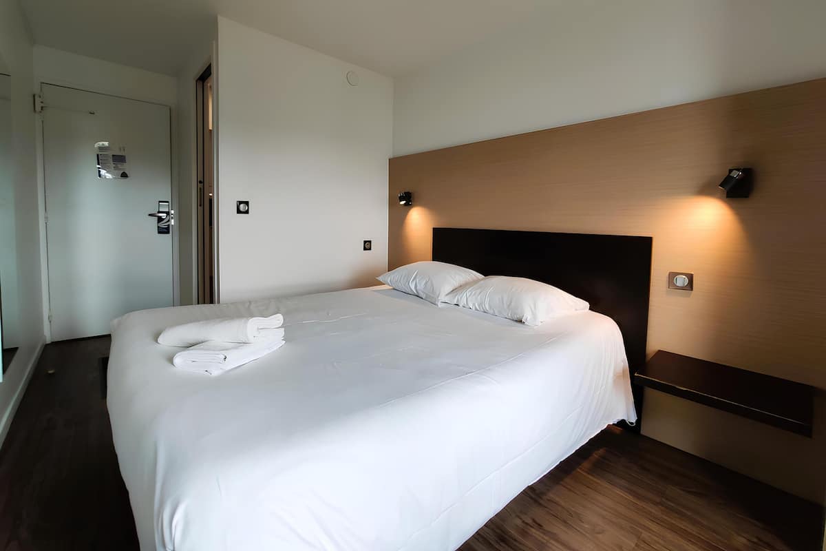 A hotel room with a neatly made bed, a wooden headboard, and a door with a handle.