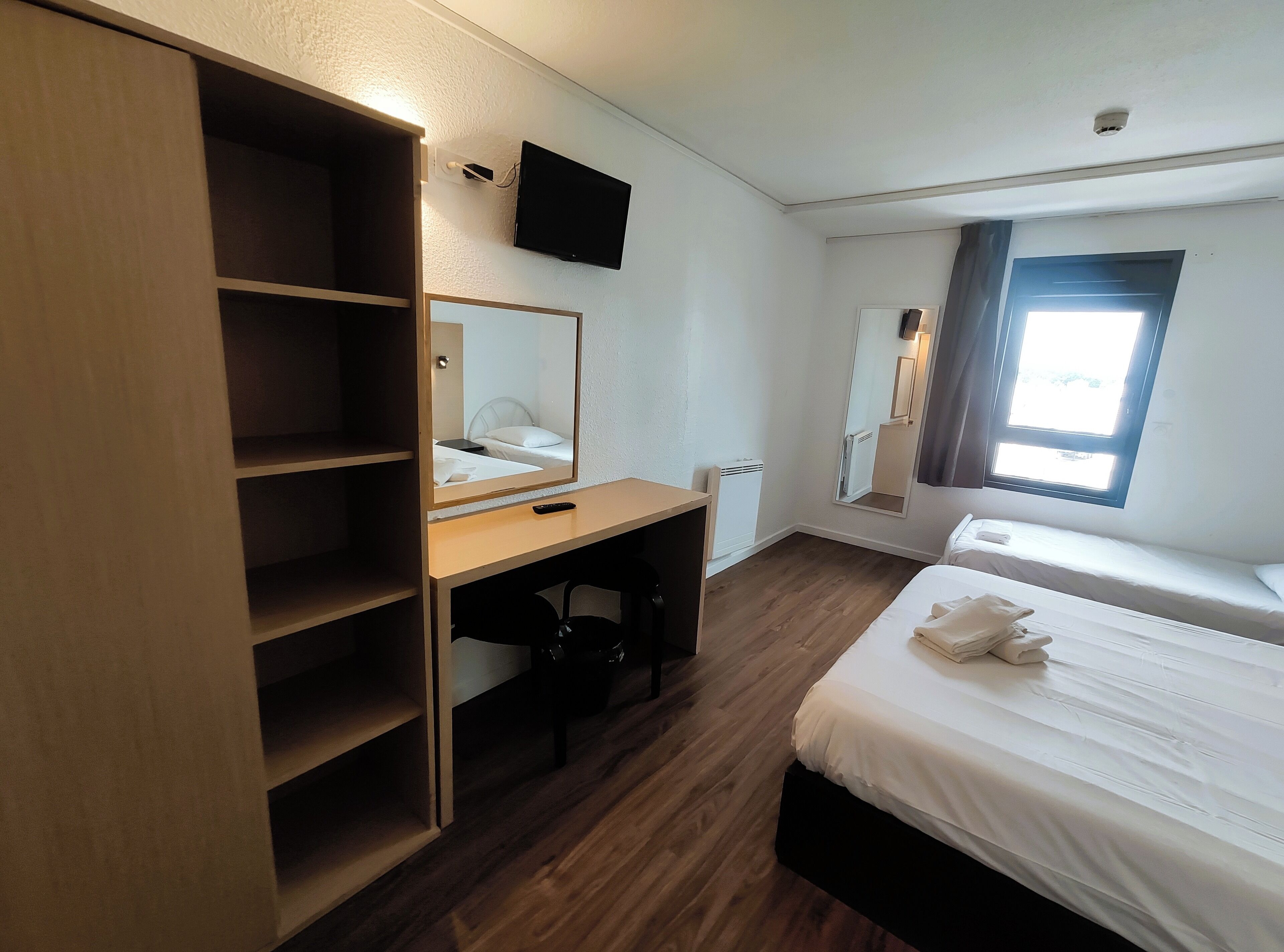 A hotel room with a bed, a desk, a wardrobe, a television, and a window.