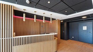 Een receptiebalie met een houten afwerking, een zwart plafond met ingebouwde verlichting, en een blauwe deur op de achtergrond.