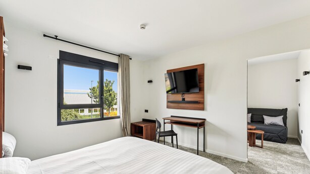Een moderne hotelkamer met een groot bed, een bureau, een aan de muur bevestigde televisie en uitzicht buiten.