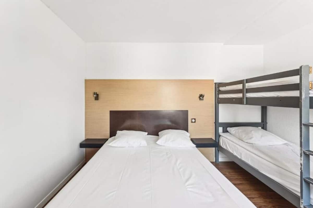 A hotel room with a bunk bed, a single bed, and a wooden headboard.