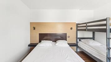 Une chambre d’hôtel avec un lit superposé, un lit simple et une tête de lit en bois.