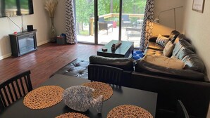 A living room with a black leather sofa, a glass coffee table, and a TV mounted on the wall. There is a sliding glass door leading to an outdoor deck with a wooden railing. - 2-bedroom condo in beautiful Fairfield Bay close to amenities. (Fairfield Bay)