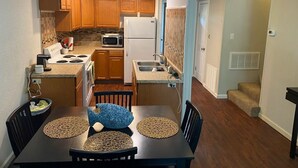 A compact kitchen with wooden cabinets, a microwave, and a refrigerator. There is a dining table with placemats and chairs. - 2-bedroom condo in beautiful Fairfield Bay close to amenities. (Fairfield Bay)