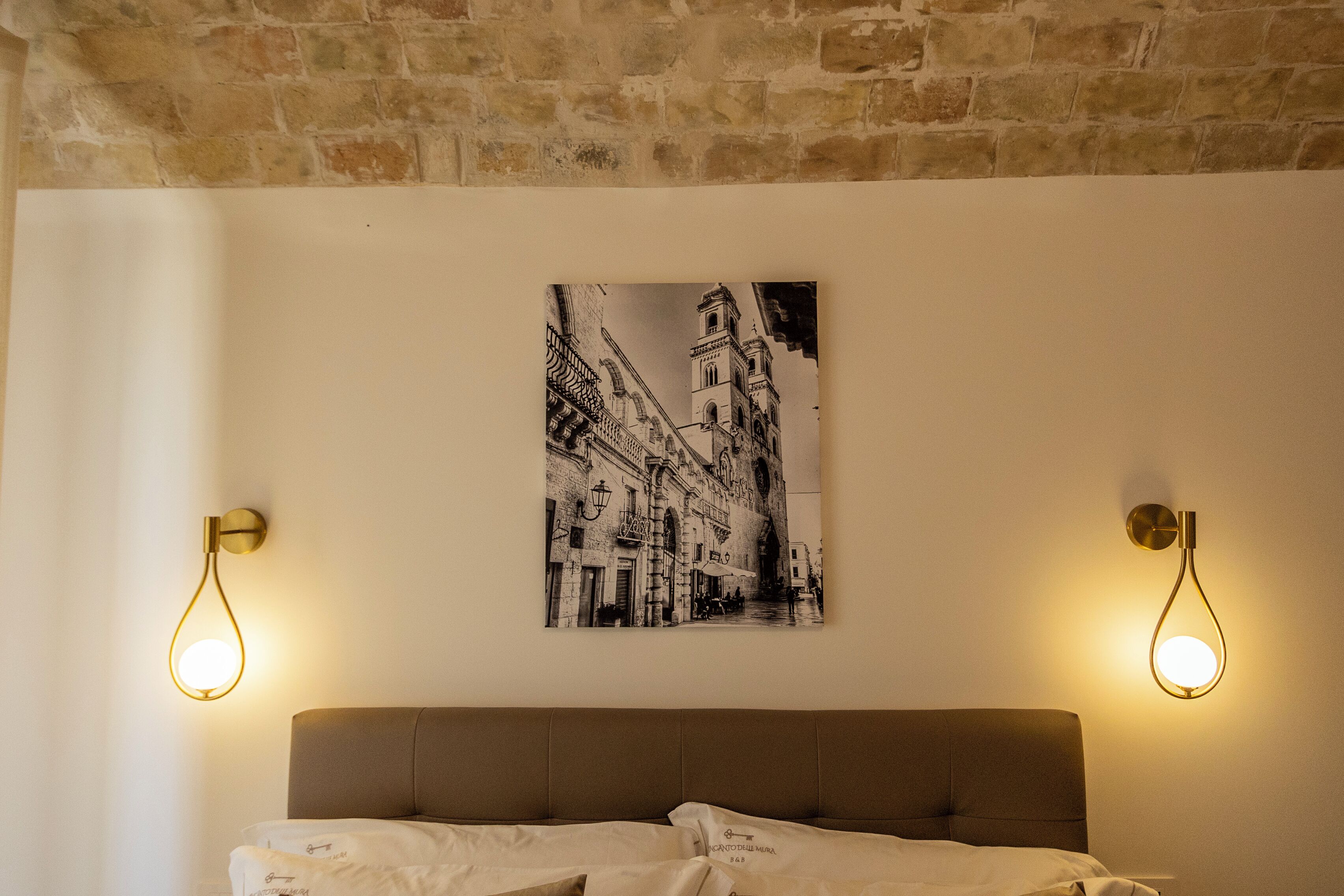 Une chambre à coucher comprenant un lit, une tête de lit, un tableau accroché au mur et deux appliques murales.