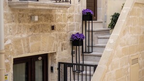 A stone building with a wooden door, a balcony with black railings, and steps leading to a second floor. - L'Incanto delle Mura (Altamura)