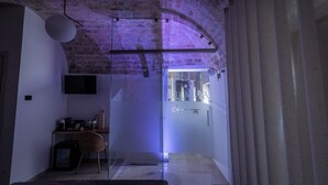 A modern room with a glass door leading to a bathroom, a desk with a chair, and a hanging light fixture. - L'Incanto delle Mura (Altamura)
