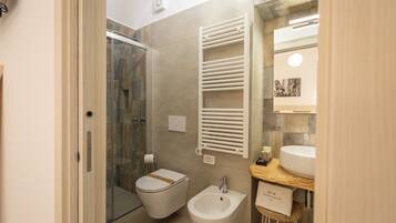 A bathroom with a glass shower enclosure, a toilet, a bidet, and a vanity with a sink.
