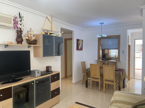 A living room with a TV, cabinets, and a dining area with chairs and a table. - 2º Line Apartment (Oropesa del Mar)
