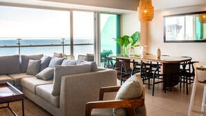 Un salon moderne comprenant un canapé, une table à manger, des chaises et une grande fenêtre donnant sur la mer.