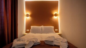 Un lit bien fait, avec deux oreillers, une table de chevet sur laquelle se trouve une lampe, et une paire de serviettes brodées du nom « Boris ».