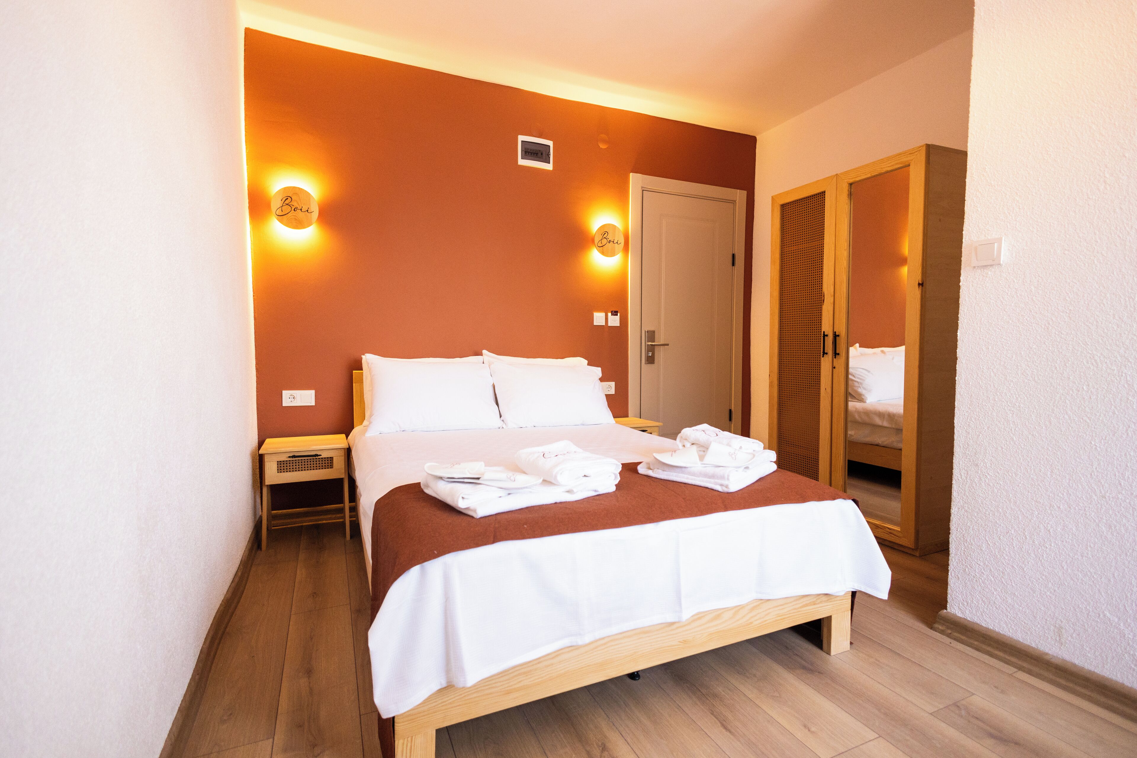 A neatly made bed with white linens and towels, a bedside table, and a wardrobe with a mirror.