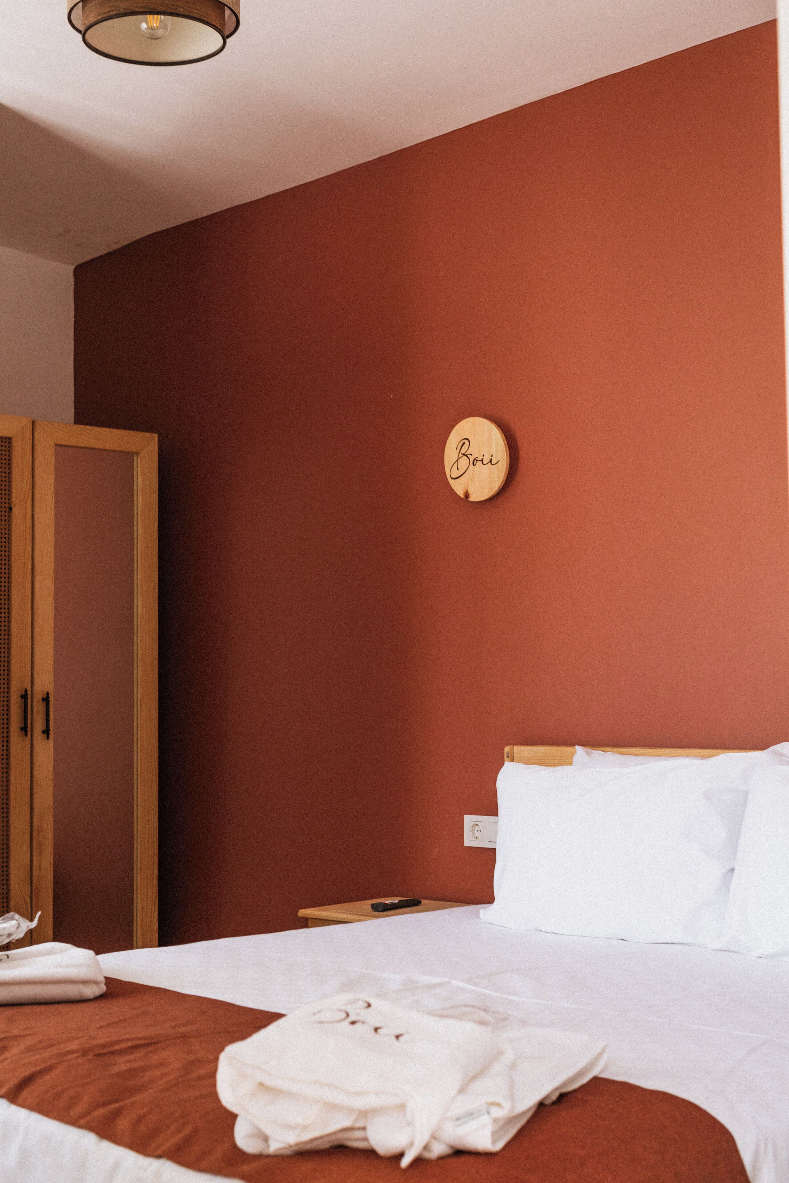 A hotel room with a bed, a wardrobe, a round wall clock, and a bedside table.