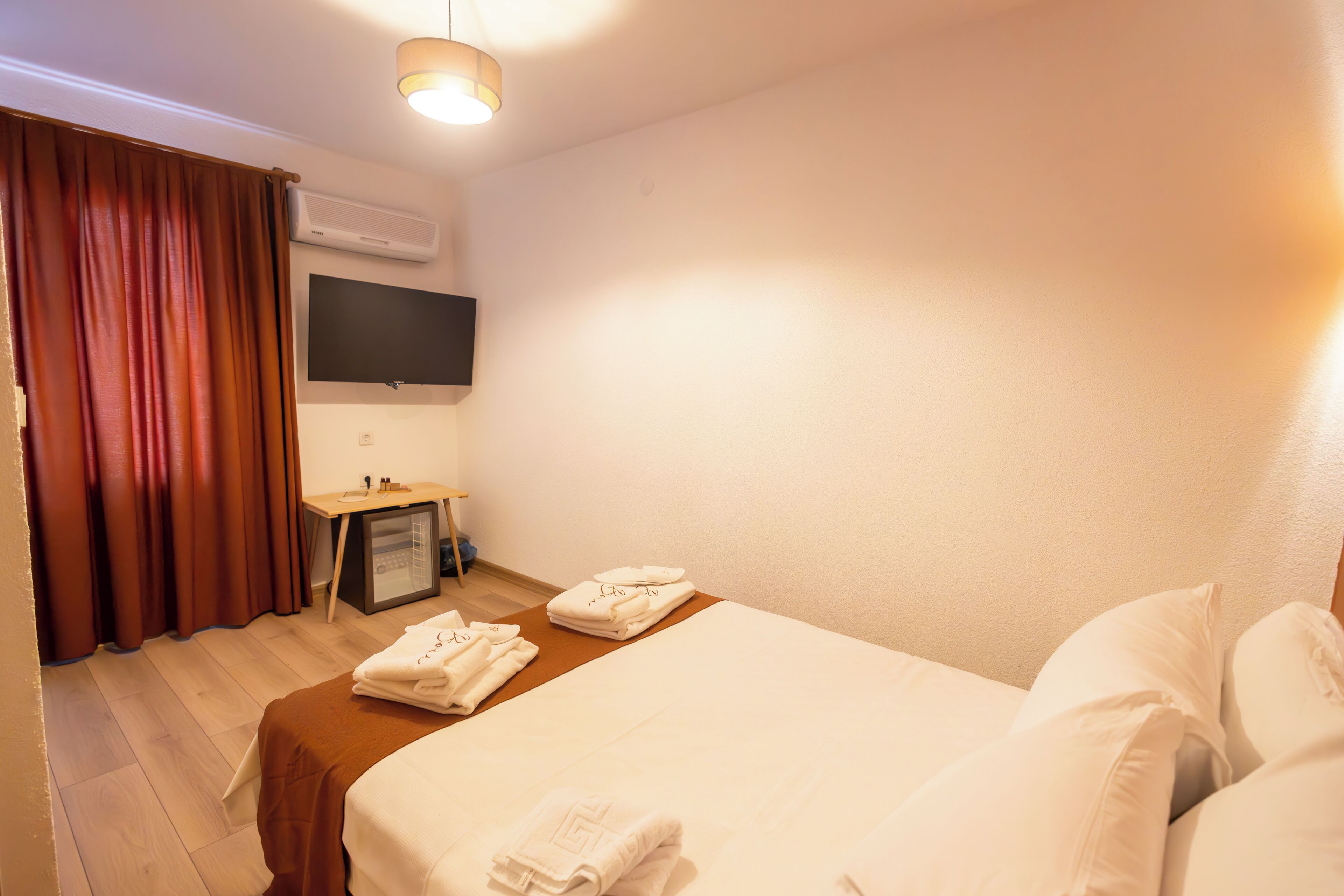A hotel room with a bed, a desk, a TV, and a minibar.