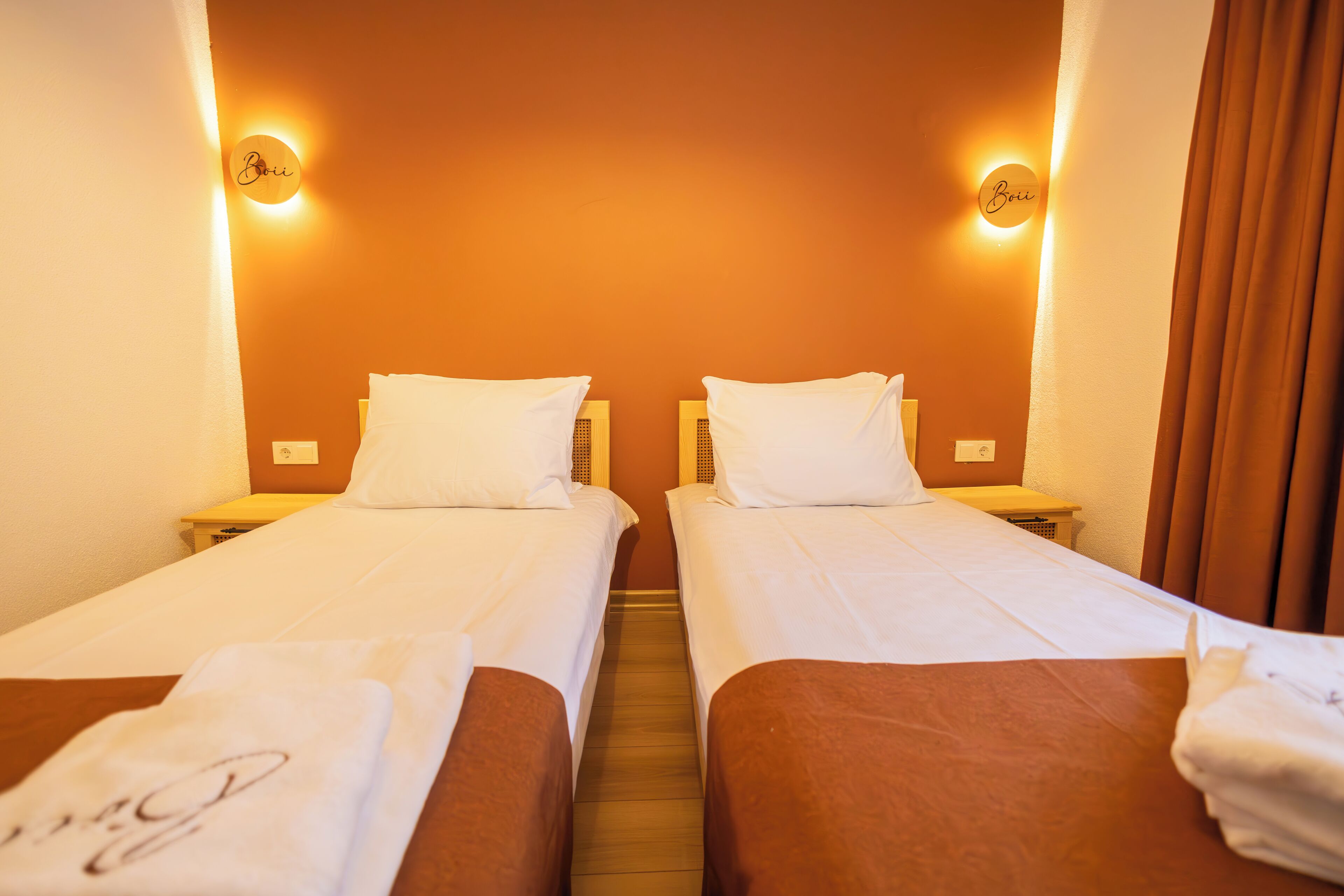 A hotel room with two single beds, each with a pillow and a nightstand.